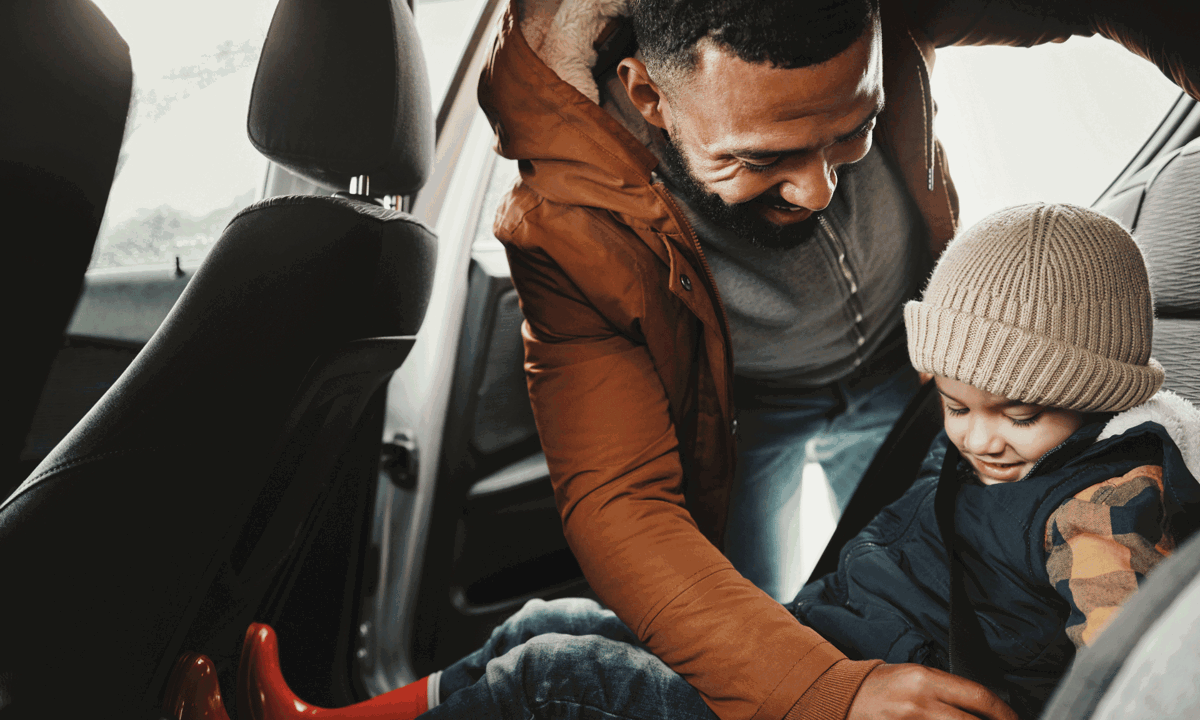 Man putting a child in the back of a car