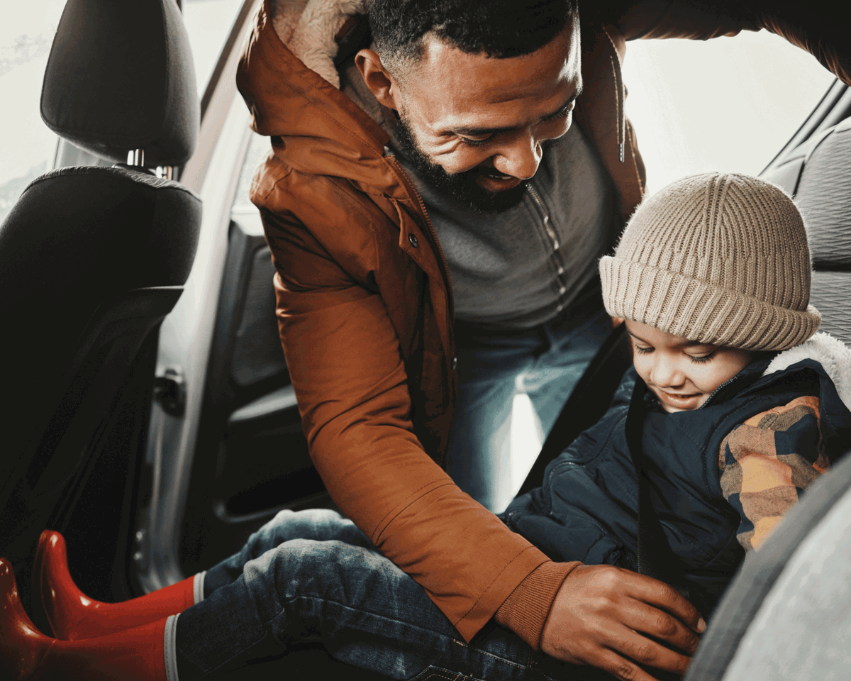 Man putting a child in the back of a car
